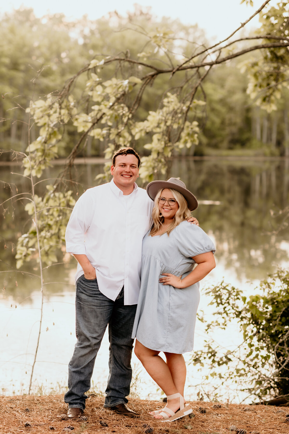 mand and woman standing together in front of a lake posing for their engagement photos in little rock