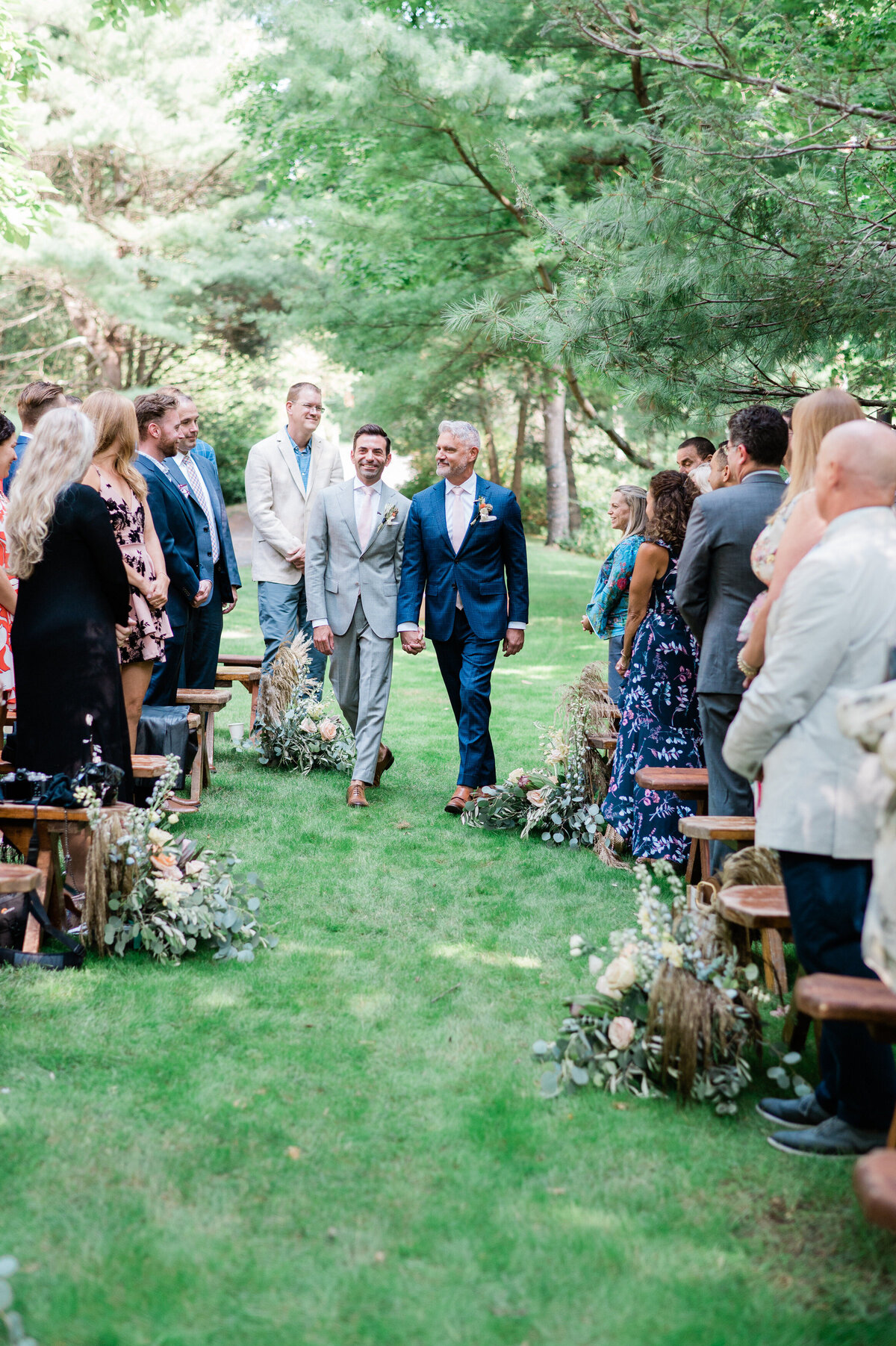 Grooms walk down the aisle together smiling 
