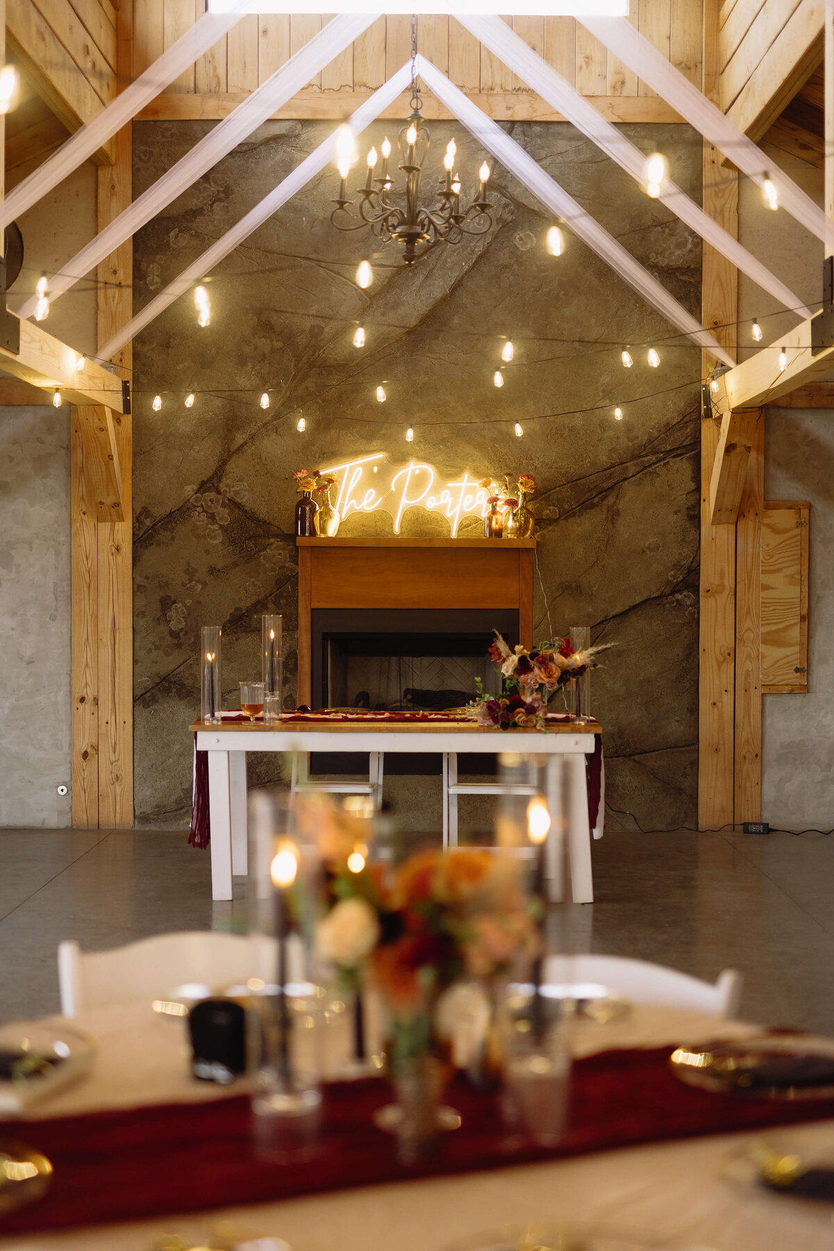 Charlottesville wedding venues indoor reception hall with white drapery and strin glights in the beams of the building with a large stone wall with a light sign of the couples last name on the stone and table scapes throughout the reception hall