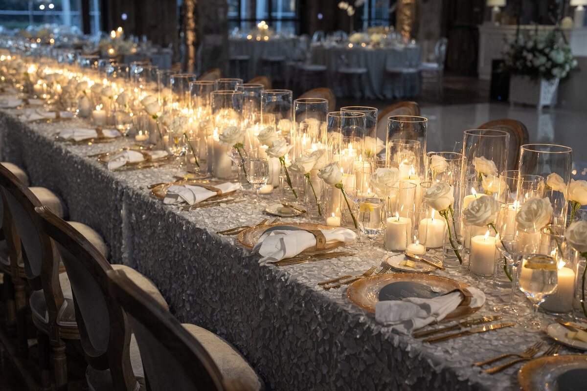 Textured floral linens, with gold lined flatware and dozens o white candles and white roses