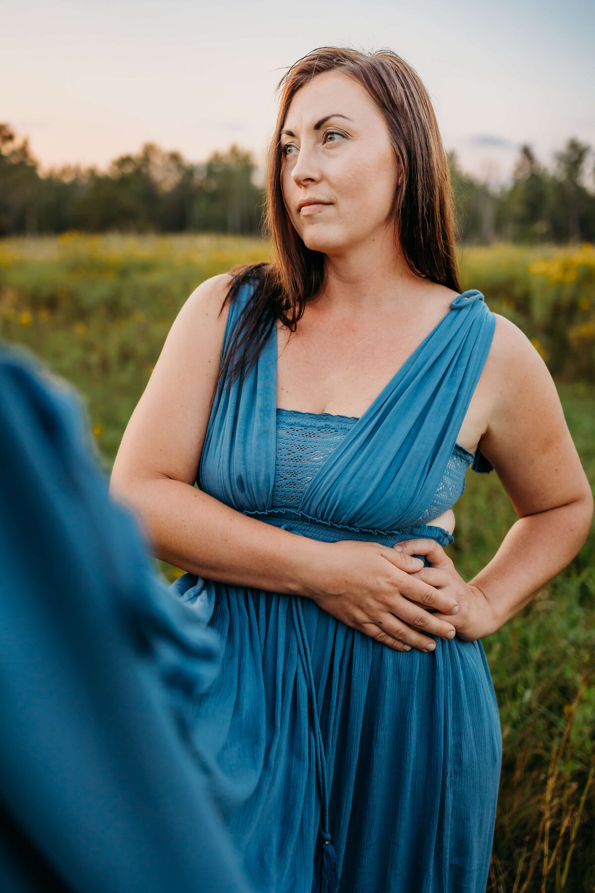 mom in blue dress in field looking off to the distance