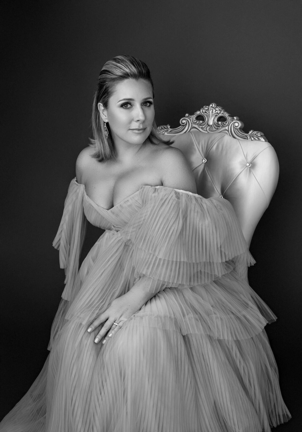 Elegant black-and-white portrait of a woman seated in a pleated gown, exuding grace and sophistication.