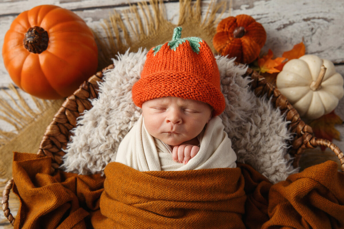 Portrait of newborn baby photographed with orange wrap and hate and little pumpkins