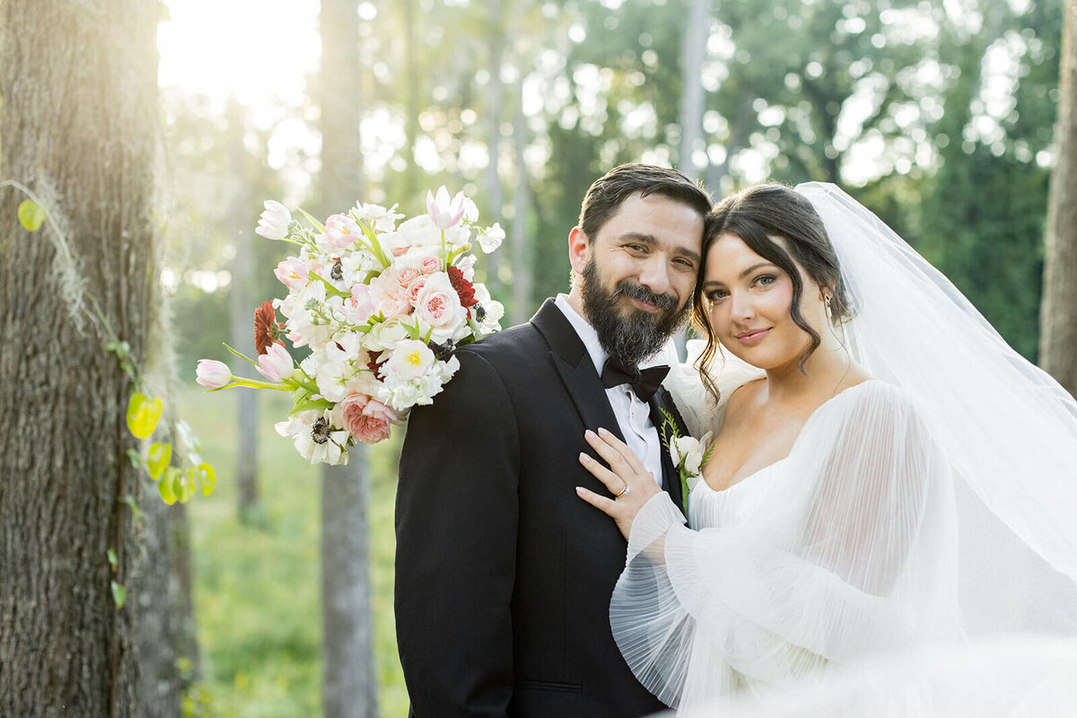 Bride and groom embrace in golden hour light at Millstone at Adams Pond, a romantic wedding venue in Columbia, SC. The bride’s flowing veil and pastel bouquet complement the groom’s classic black tuxedo, creating a timeless and elegant wedding portrait.