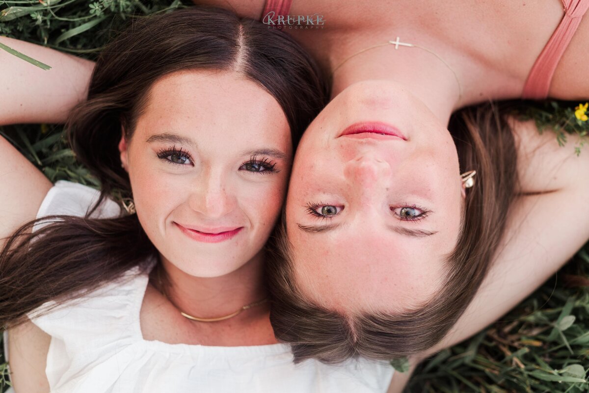 two girls laying in the grass with their faces touching