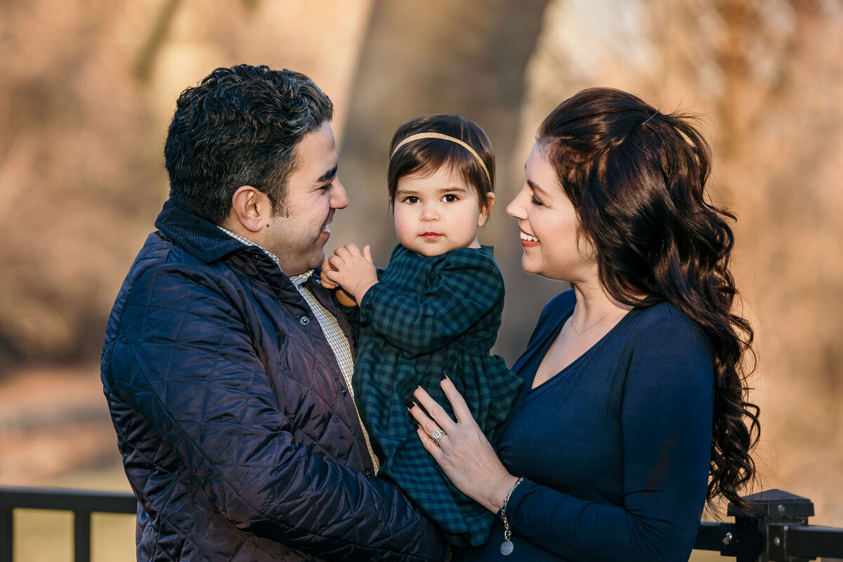 mom and dad in navy winter clotheslaughing with their one year old daughter in the winter at a family session
