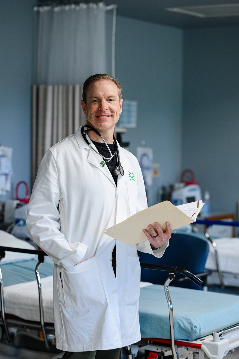 A doctor stands in a hospital holding a chart and smiling at a Denver band photographer and commercial photographer in Denver for branding photos and a brand photography photo shoot.