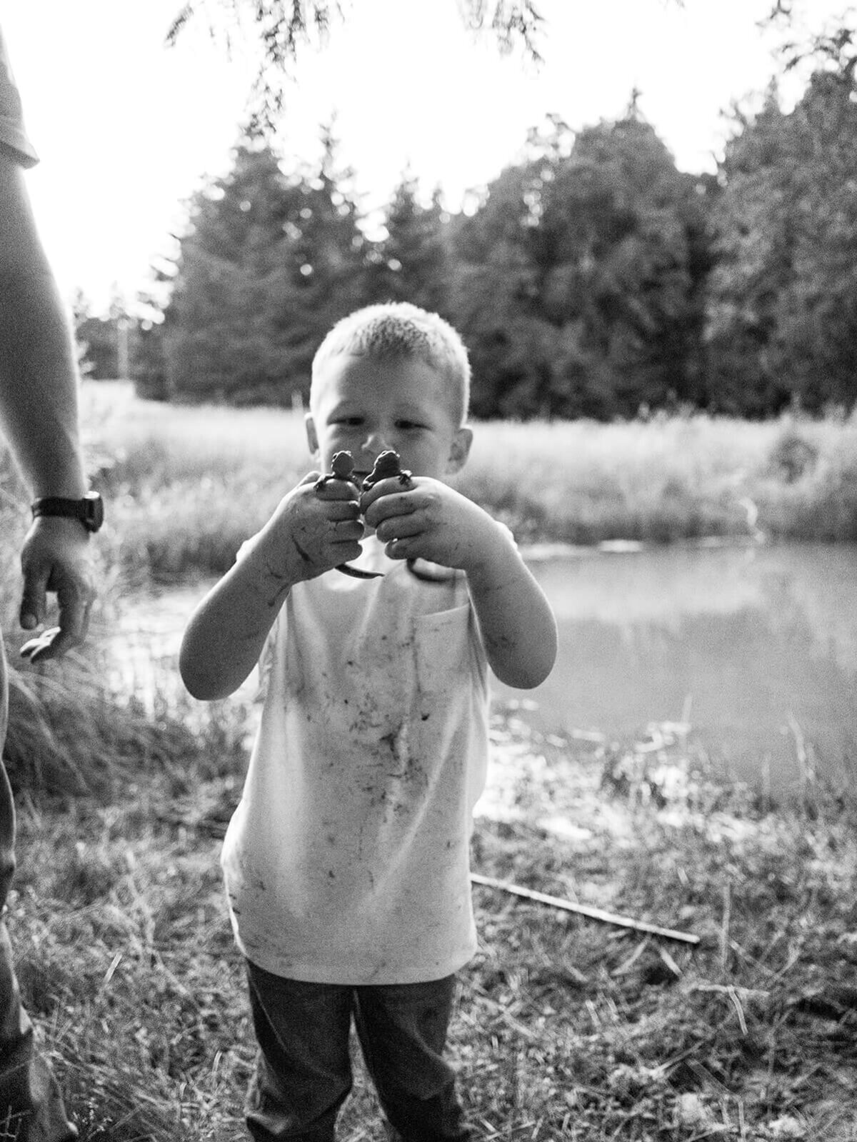 A young boy holds up lizards in each of his hands.
