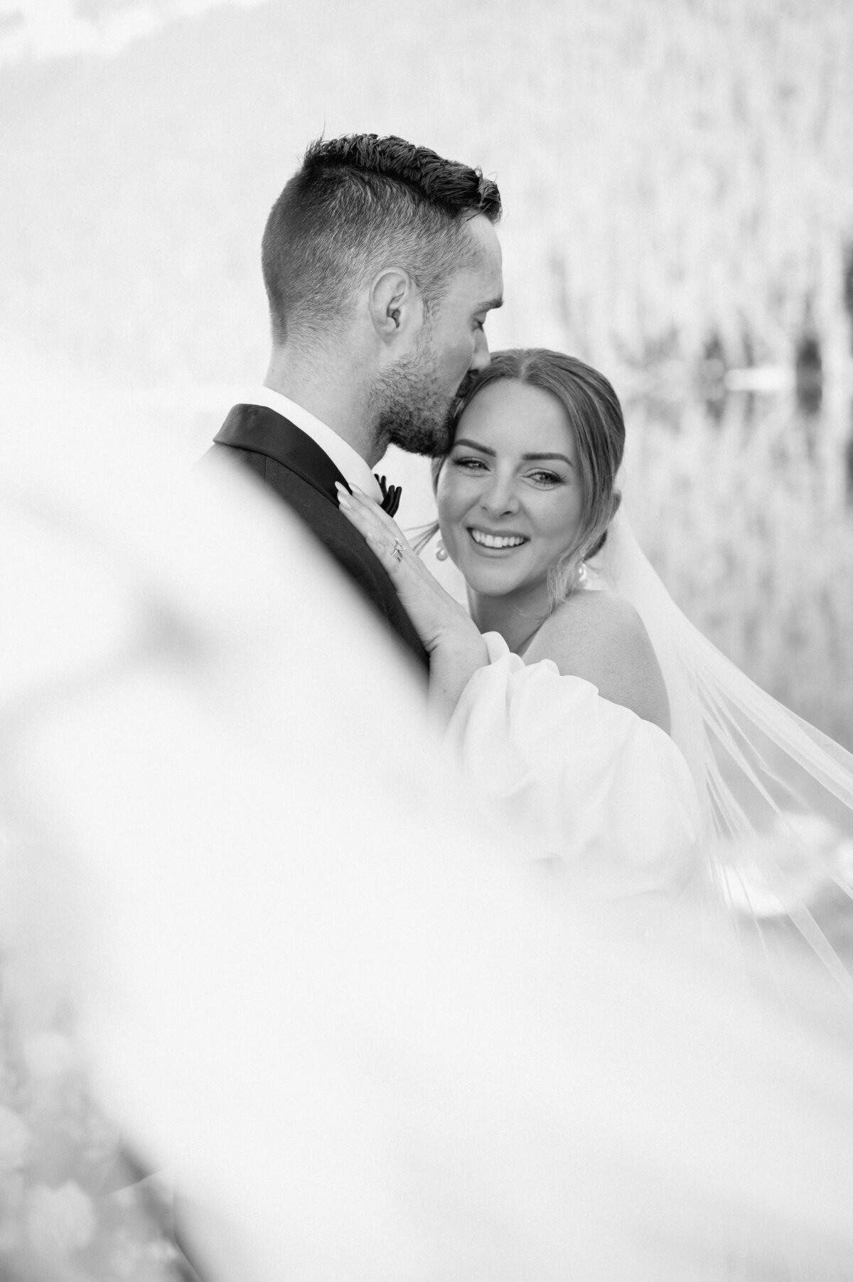 Black and white photo of bride smiling while hugging groom