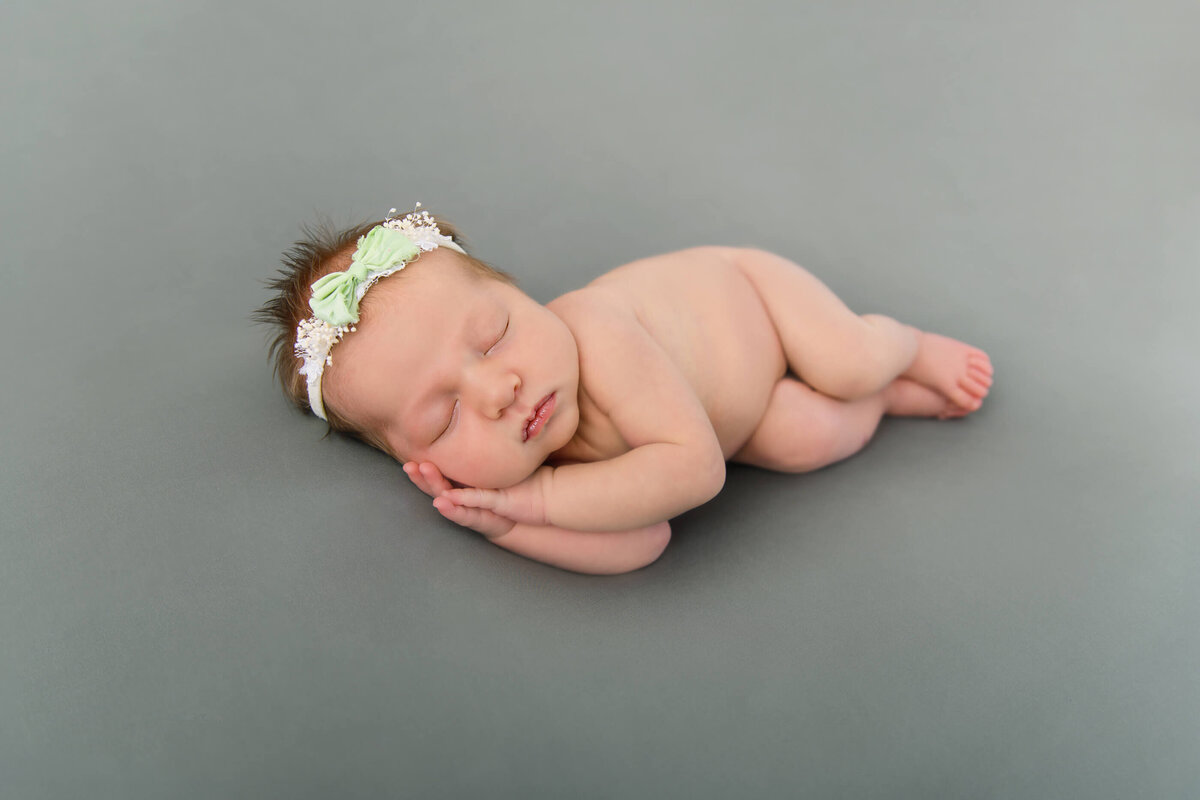 newborn baby girl laying on her side on a green background for her Burlington newborn photography session.