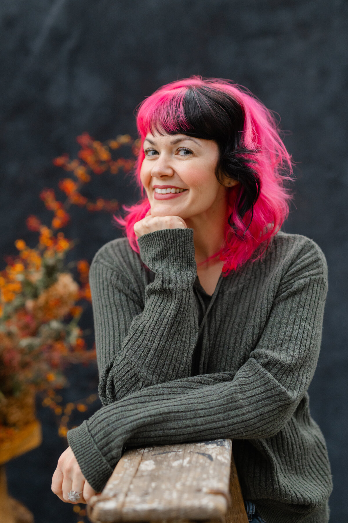 Lady with pink and black hair with hand under chin