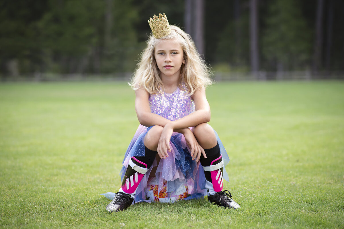 Girl sitting on a soccer ball with tiara  and dress