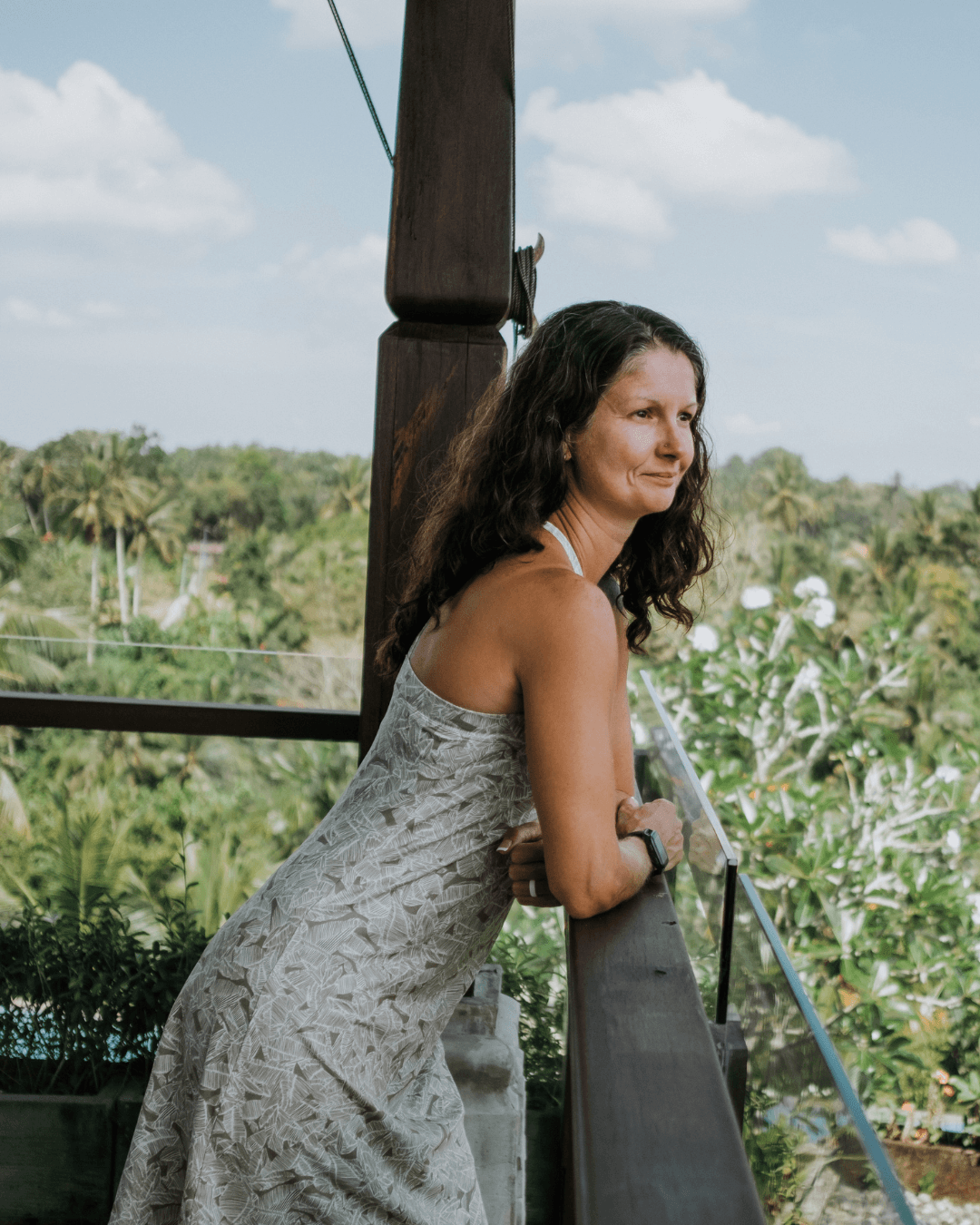 Rachel Cline leaning on a wooden railing outdoors, looking out over a garden
