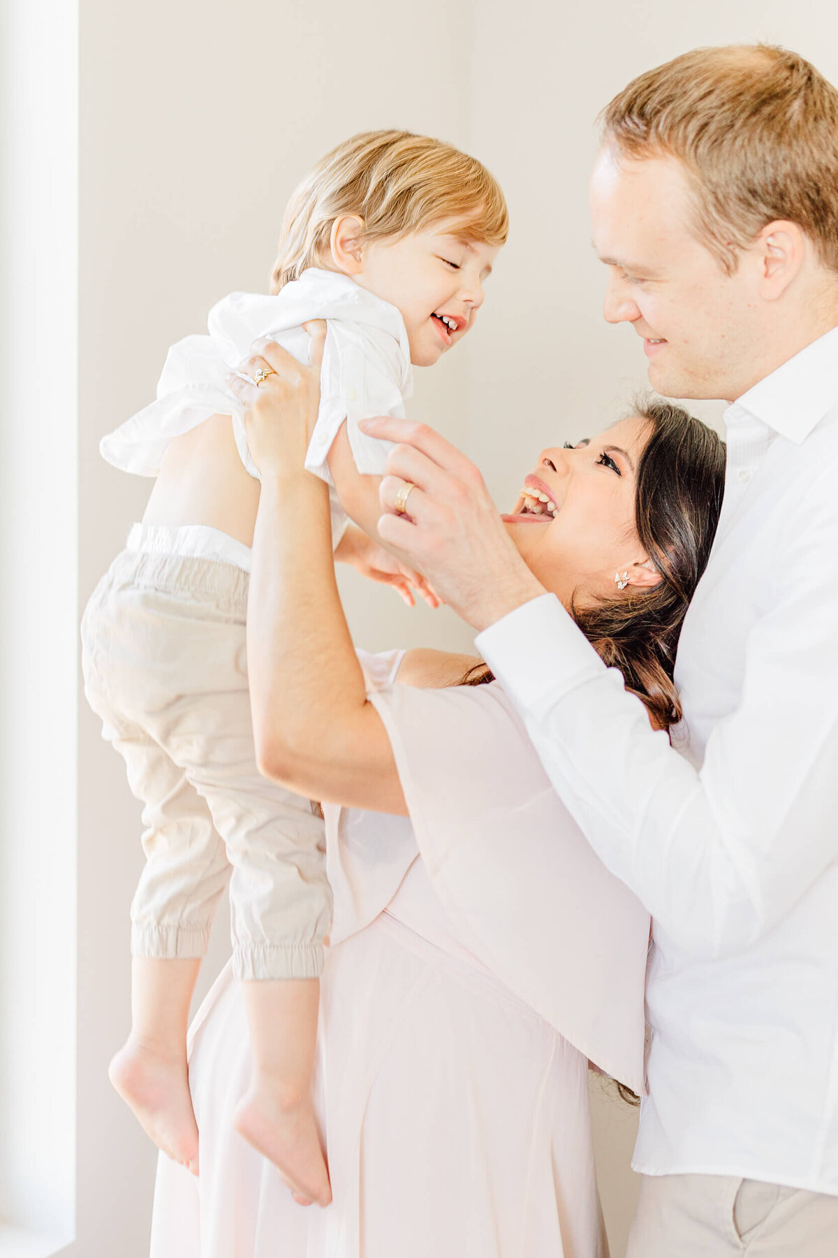 Pregnant mother and her husband hold up their laughing toddler in the air