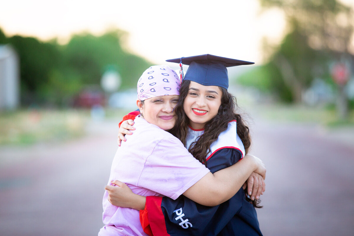 Senior girl in cap & gown hugging mom in middle of rd