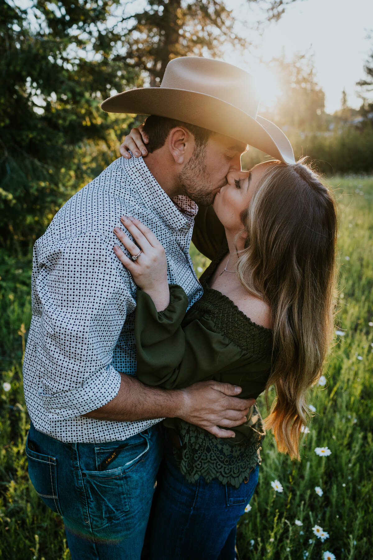 Couple embrace each other and kiss while sun sets behind his cowboy hat.