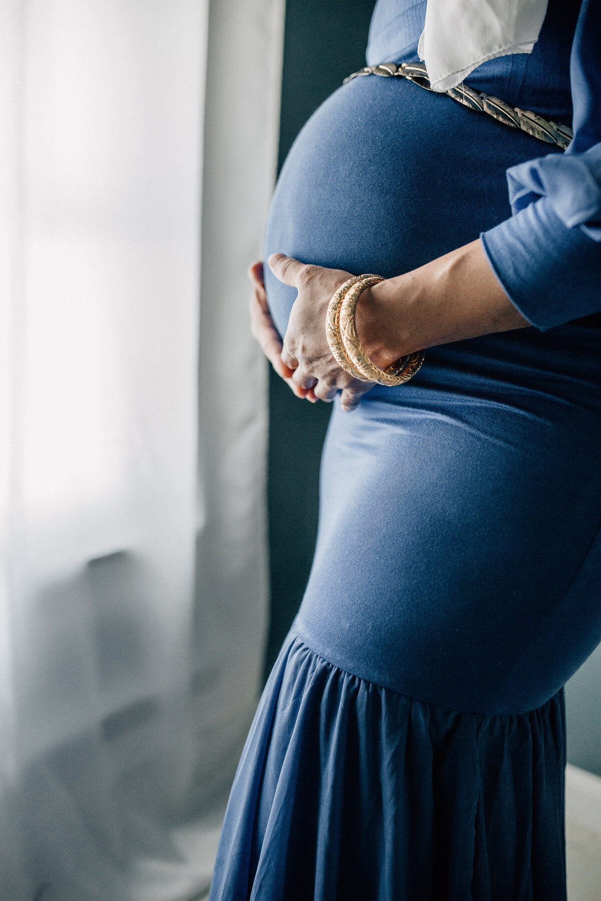 Maternity shot of a mom wearing blues dress holding belly.