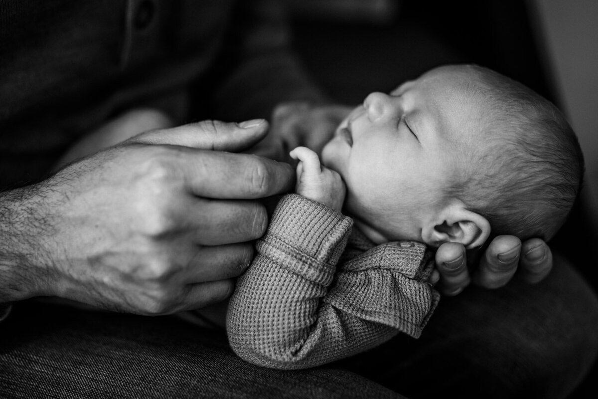 profile of baby sleeping in Dad's hand and baby's hand wrapped around finger