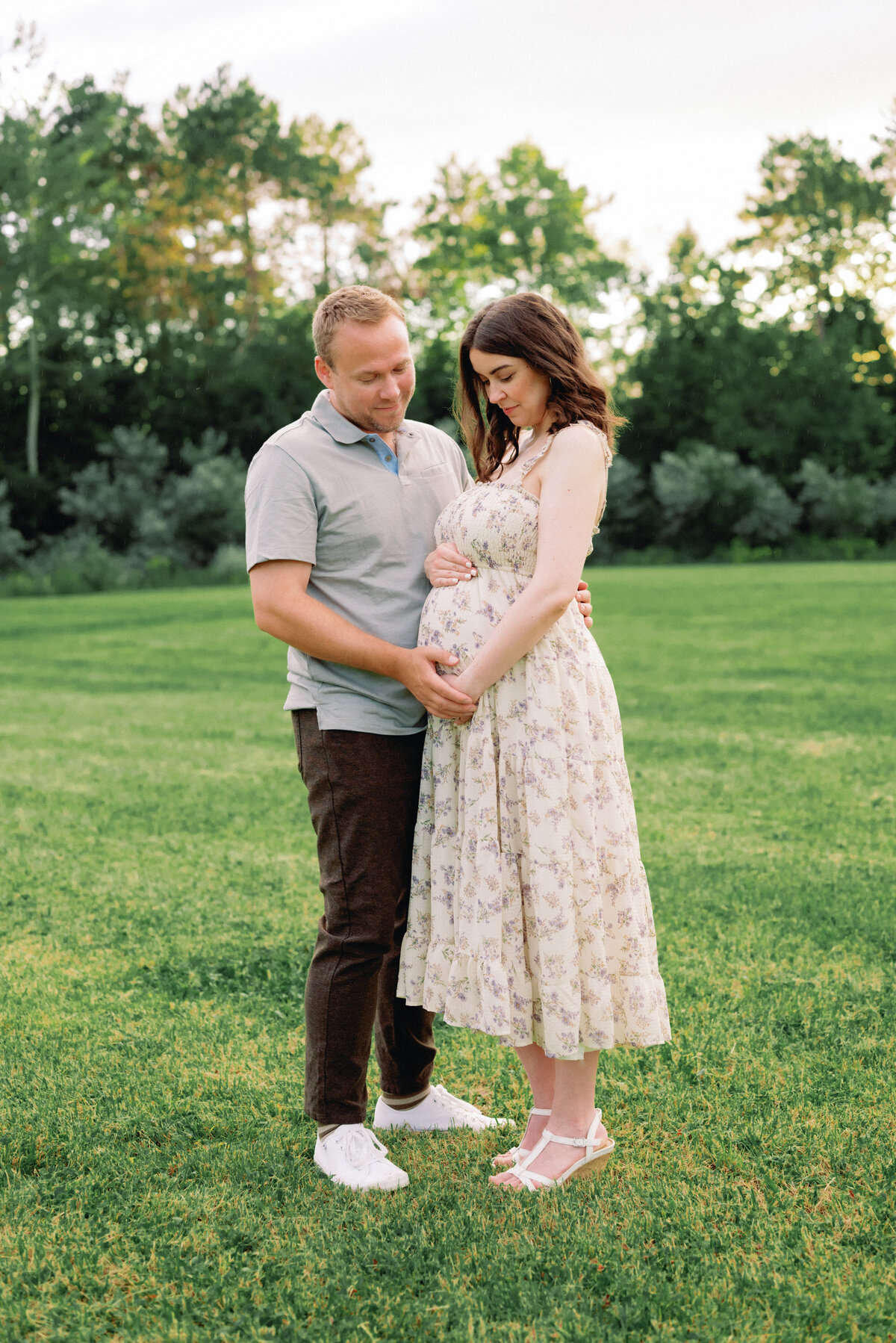 Father looking down at baby bump for mother in floral dress