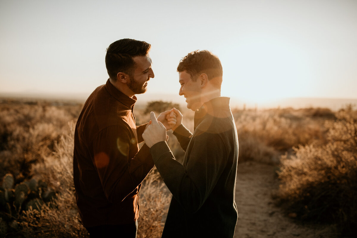 two men holding hands and laughing in the desert