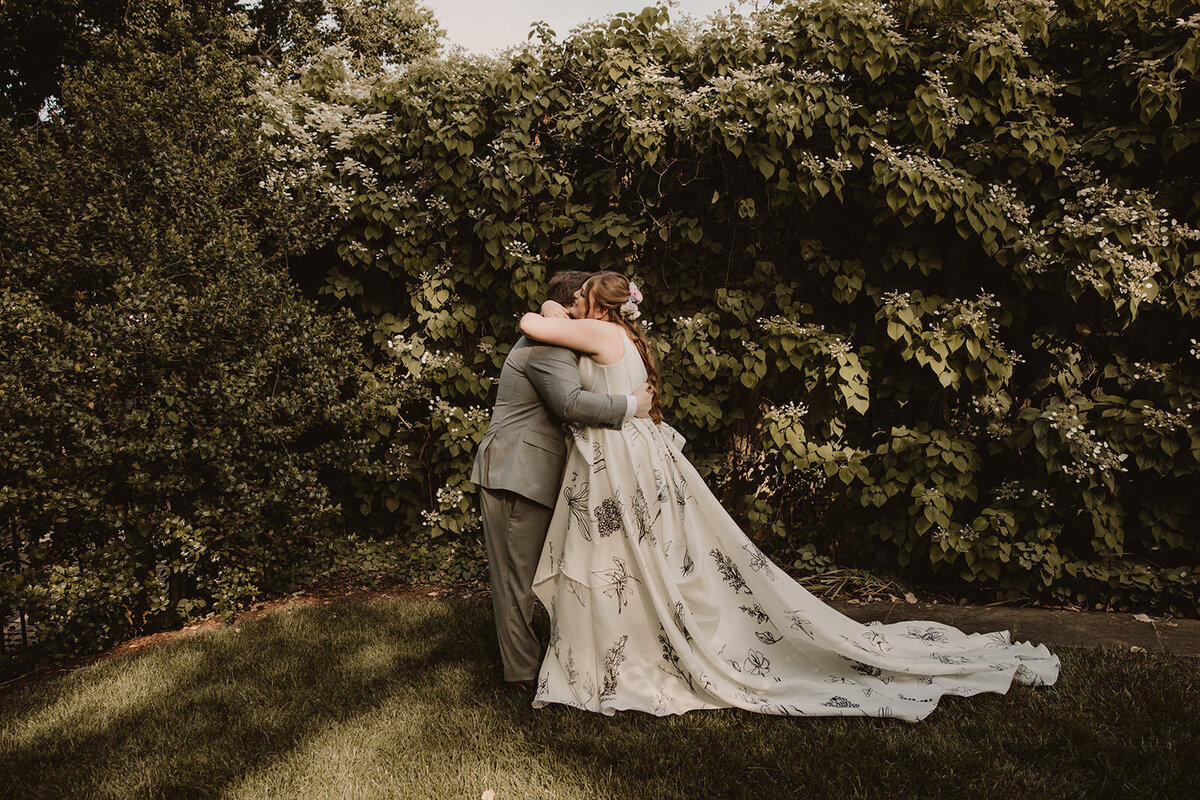 A wedding couple hugging while standing in a wooded area 