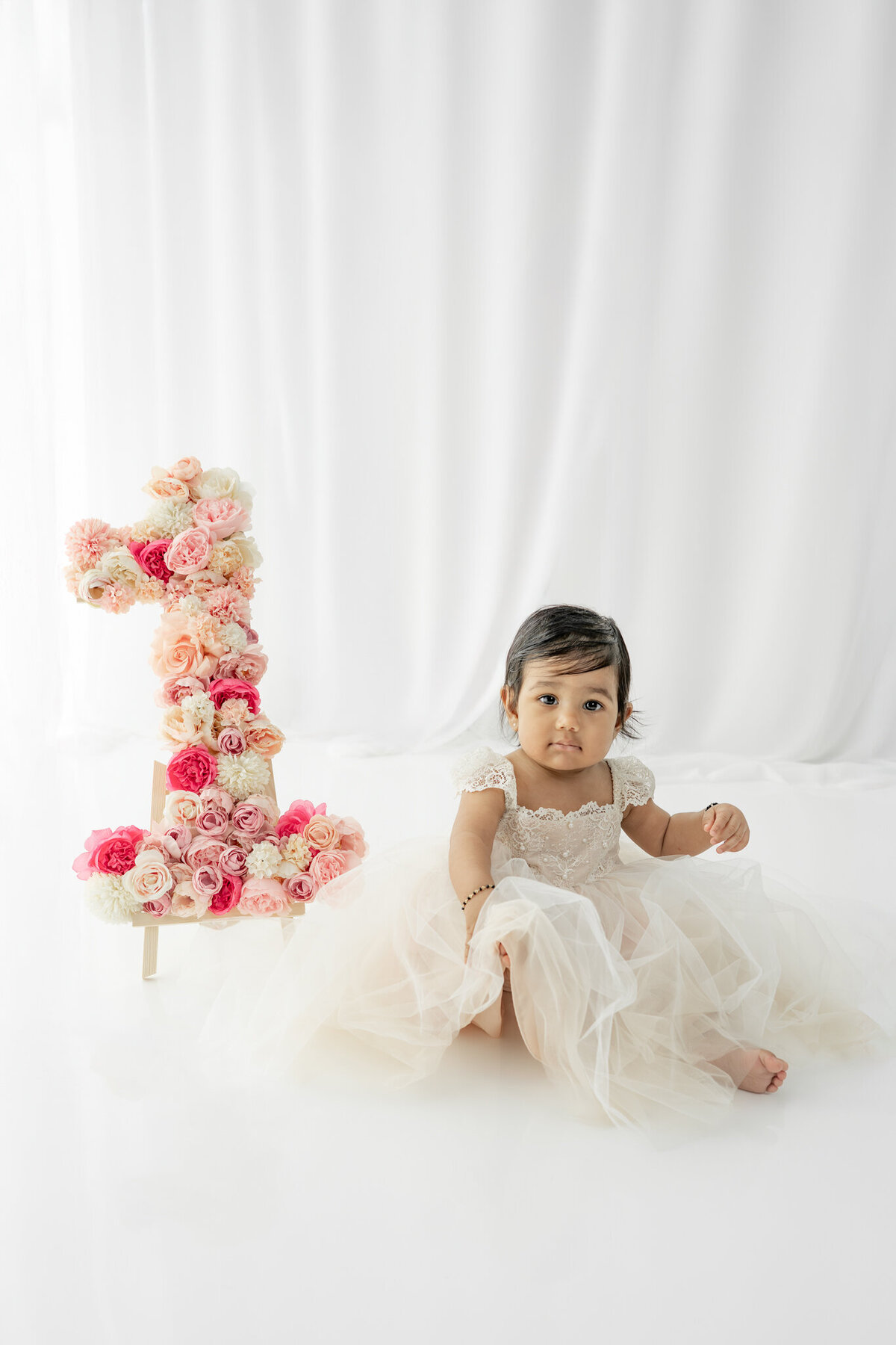 Girl in dress sitting next to floral 1 during a cake smash session— captured by Alliston and Barrie cake smash photographer.