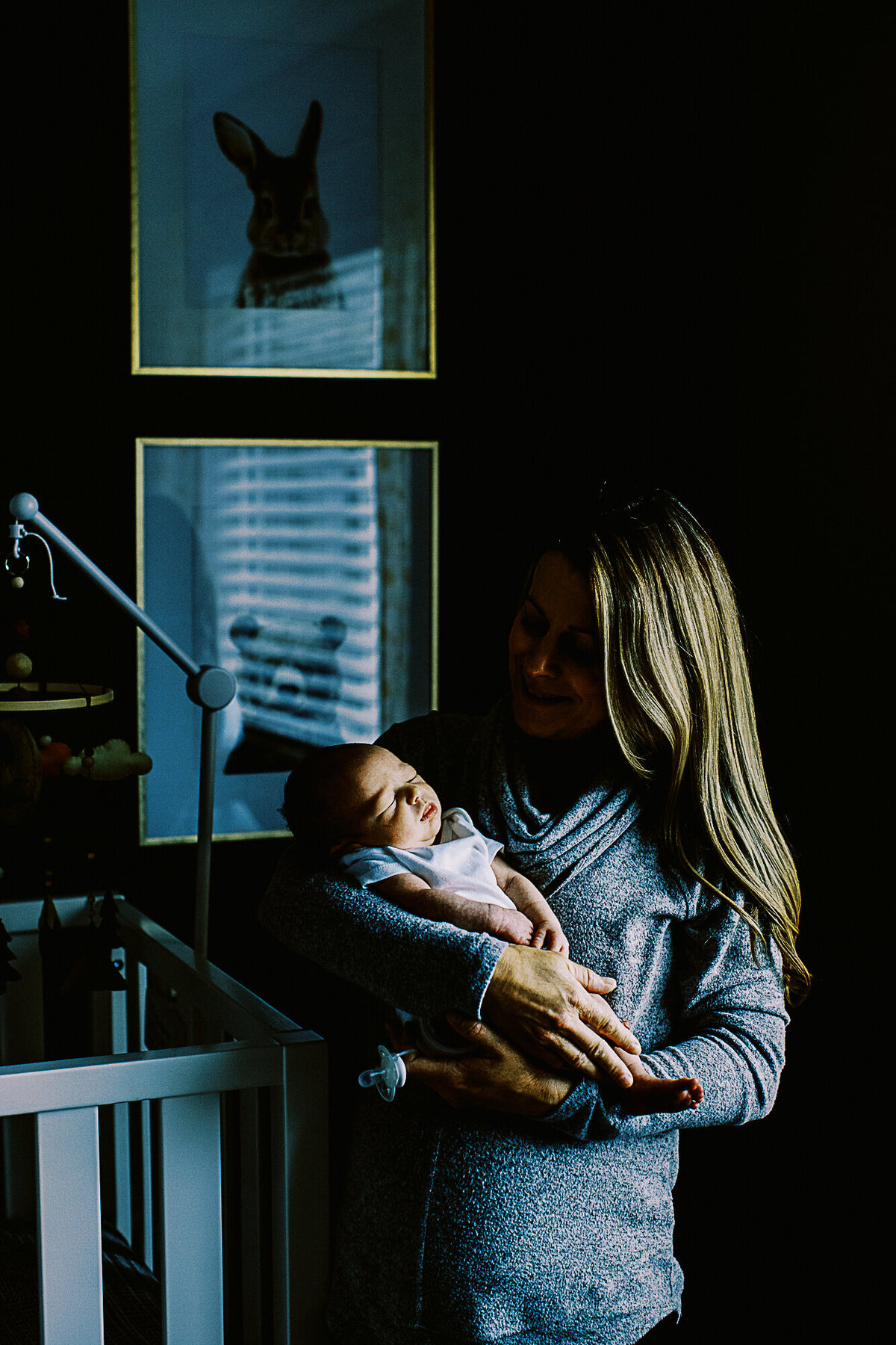 mom with long blonde hair stands and holds baby boy