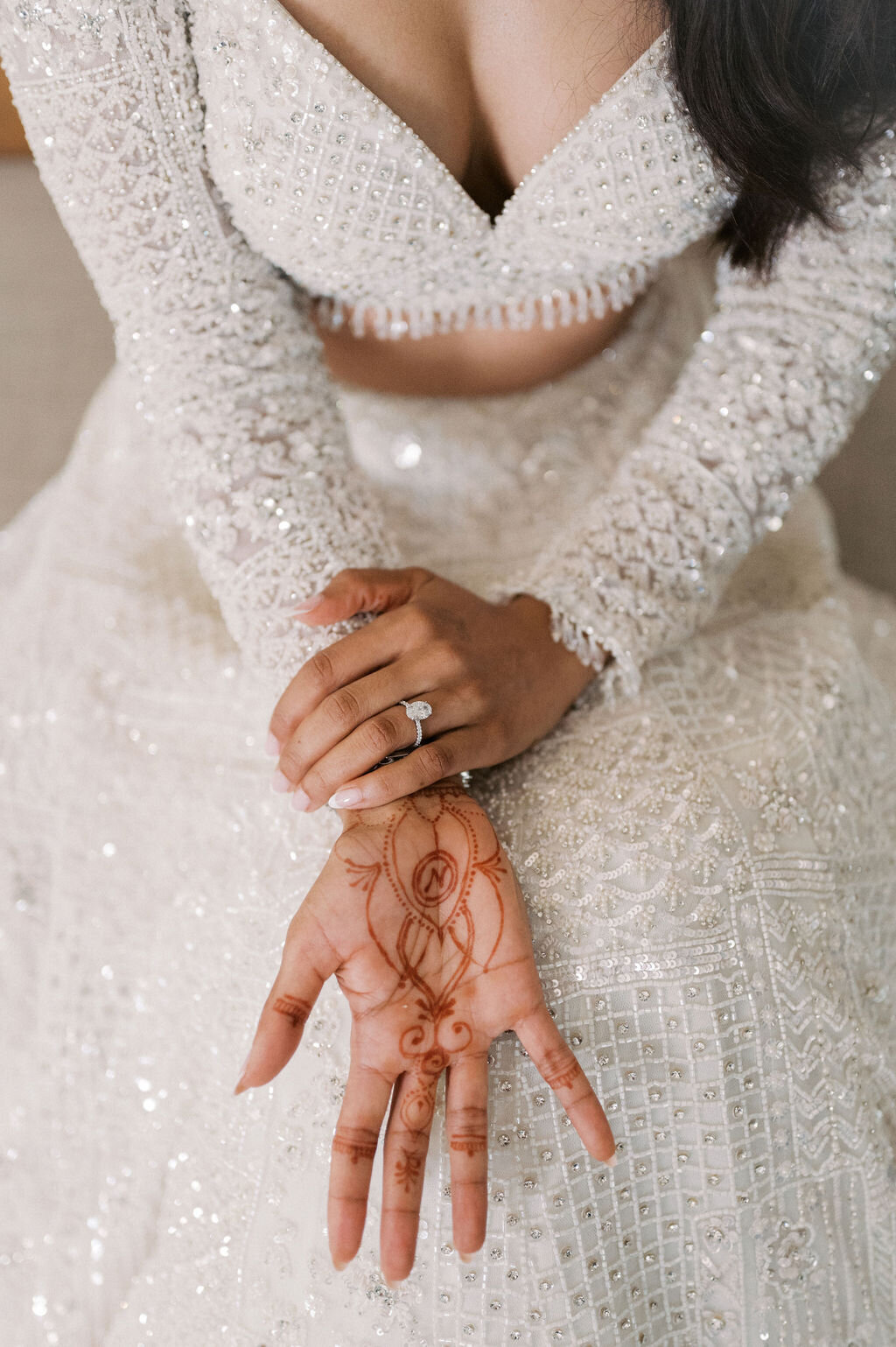 Close-up of bride’s henna design and engagement ring against her beaded bridal gown.
