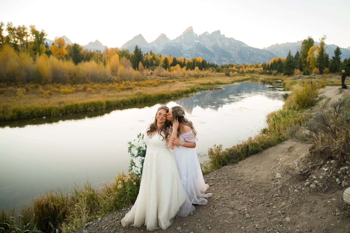 Bride and bride share a kiss in front of the grand tetons at swabacher's landing