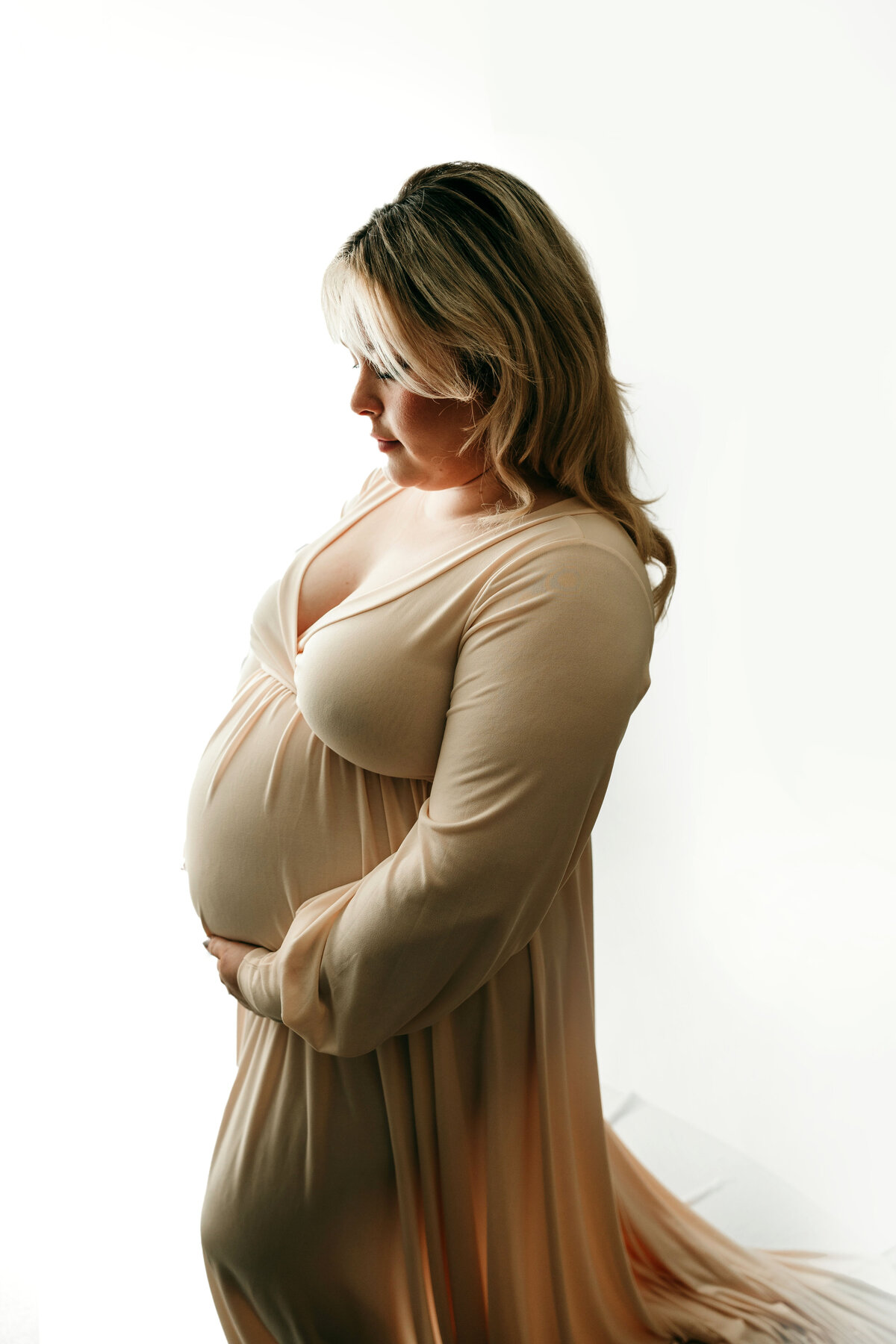 An expecting mother holds her growing stomach in a flowy tan dress.