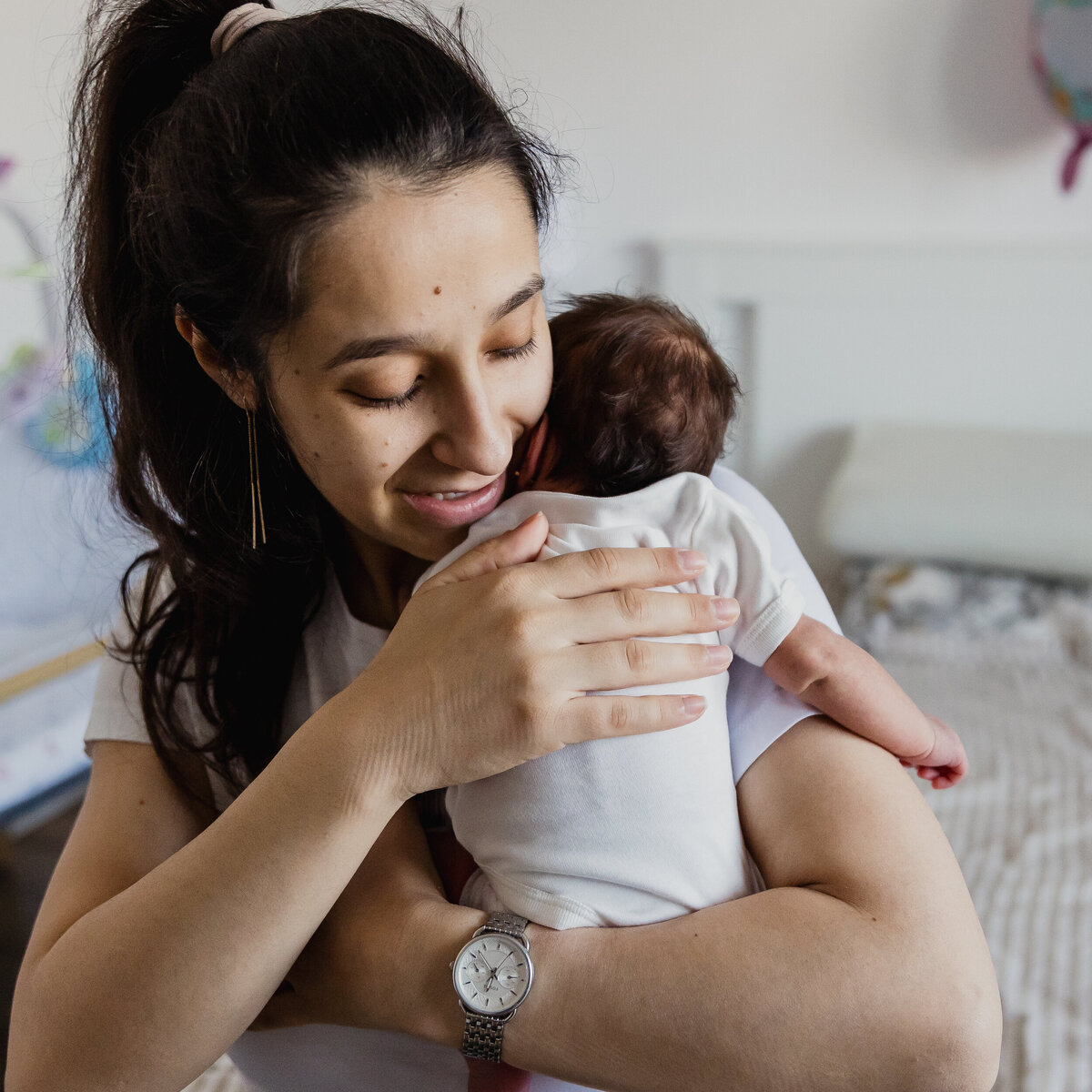 A mother gently holds her newborn baby in a cozy room, both enjoying a serene and affectionate moment together.