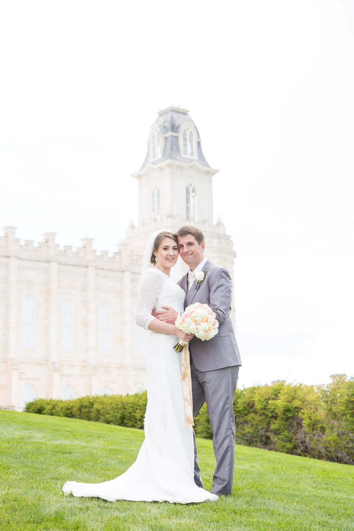 classic wedding portrait of bride in lace dress and and groom  in gray suit on hill by the Manti Utah lds temple