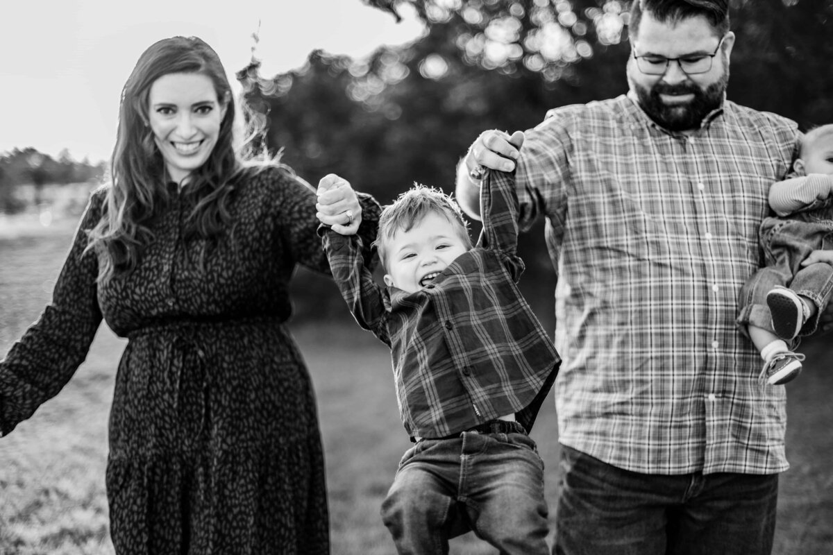 Austin, TX family of four. Mom and dad are swinging their three year old son between them while dad holds newborn son.