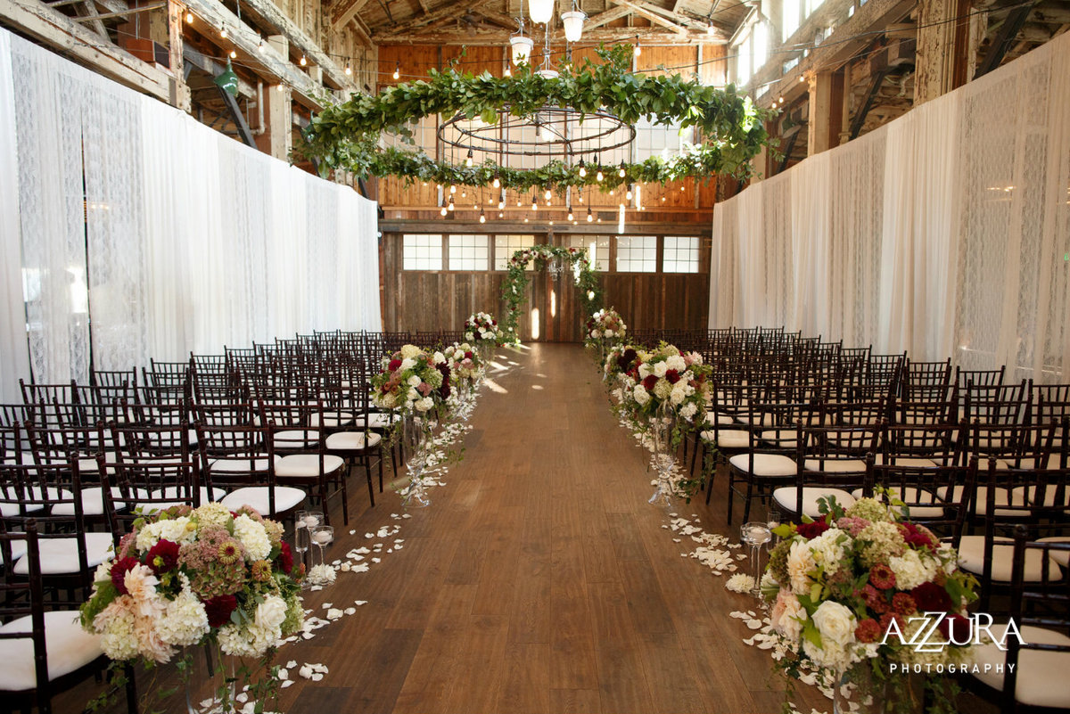 Sodo Park wedding with large greenery ceiling wreath and ceremony aisle lined with large flower arrangements