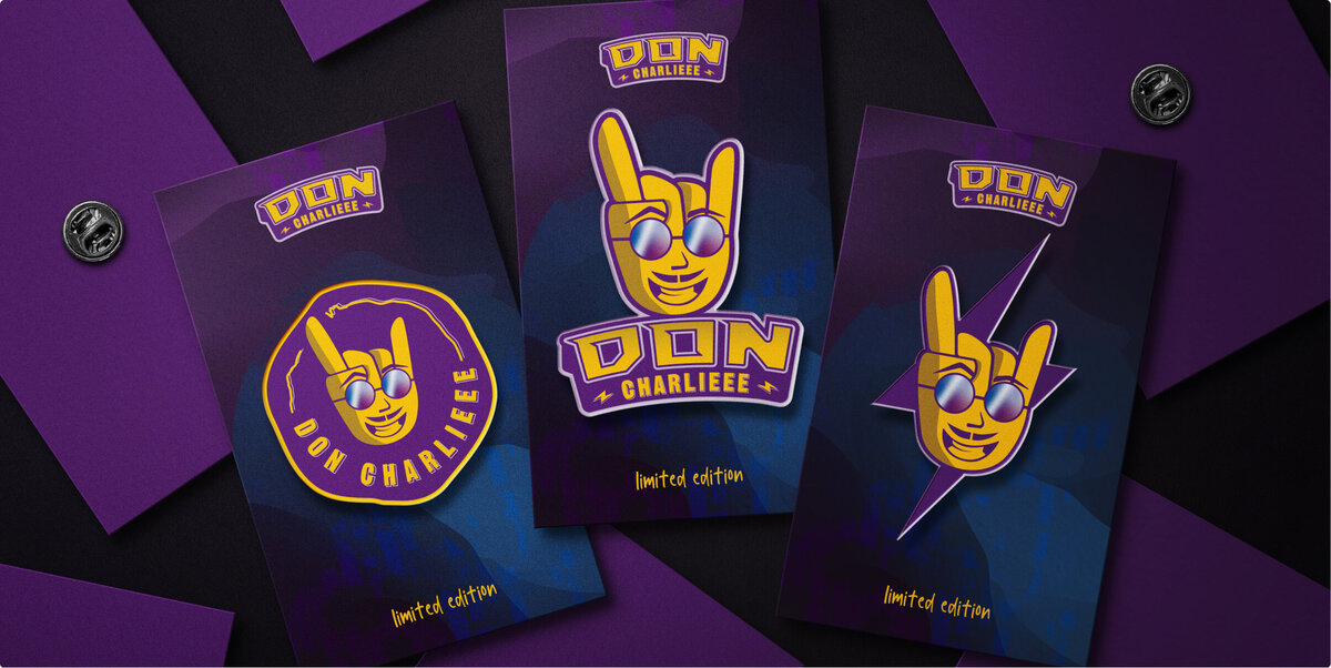 An array of enamel pins with three designs on the forefront: rock hand symbol with a smiling face wearing reflective sunglasses. The brand name is Don Charlieee.