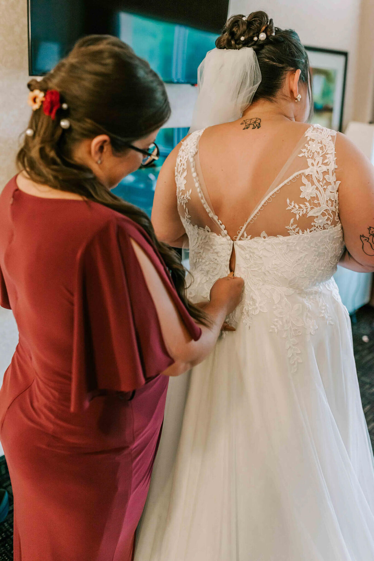 Bridesmaid zipping up brides dress.