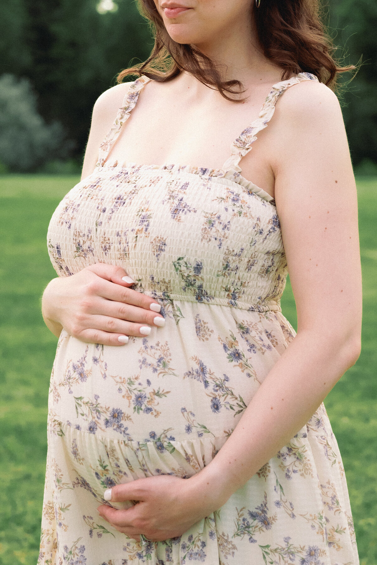 Close up of mother holding baby bump in floral dress