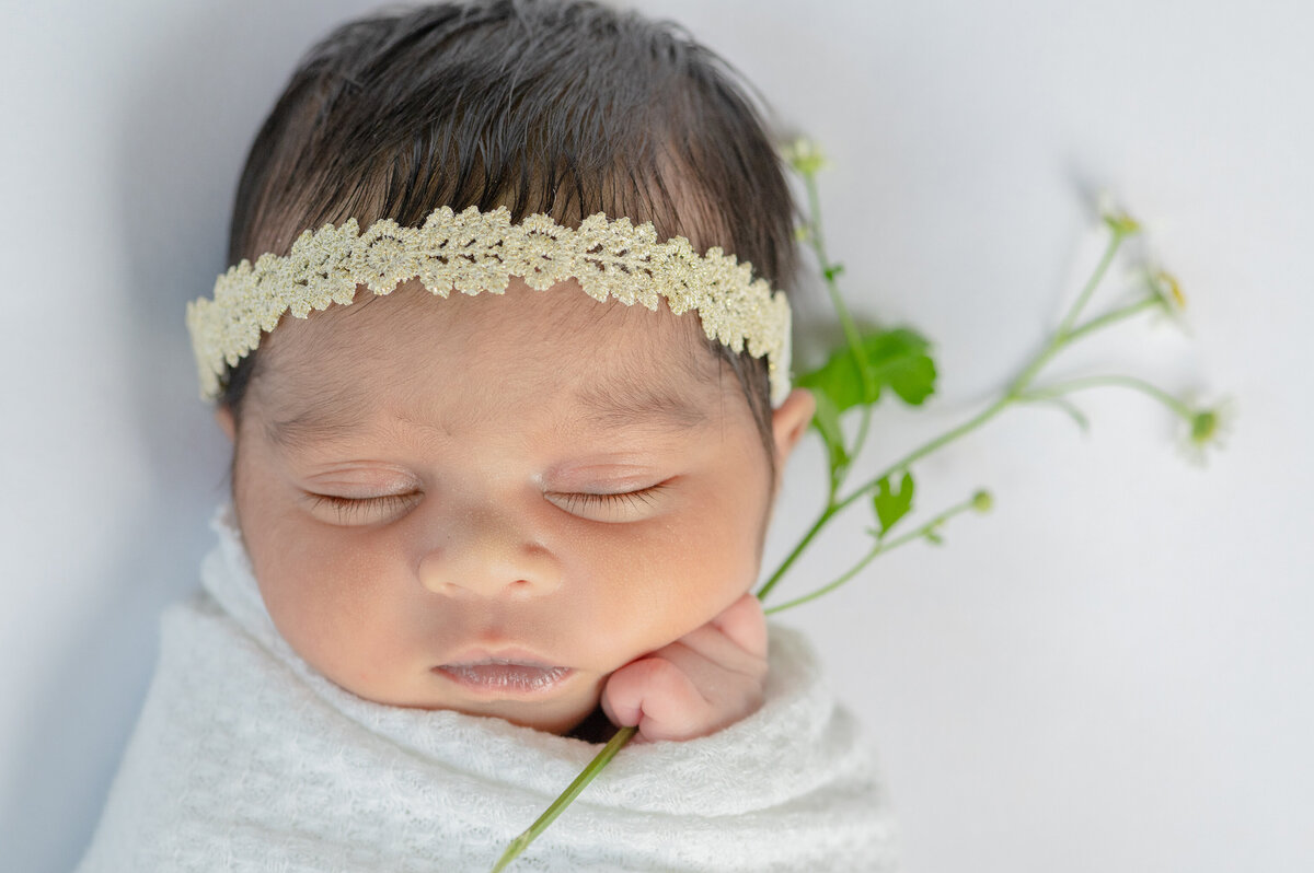 Newborn baby holding a flower with a gold headband.