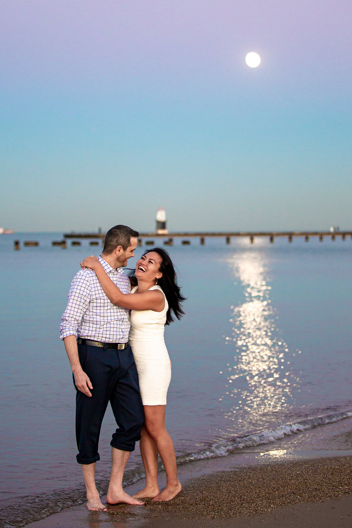 An engaged couple laugh during a sunset engagement photo on a beach in Chicago.