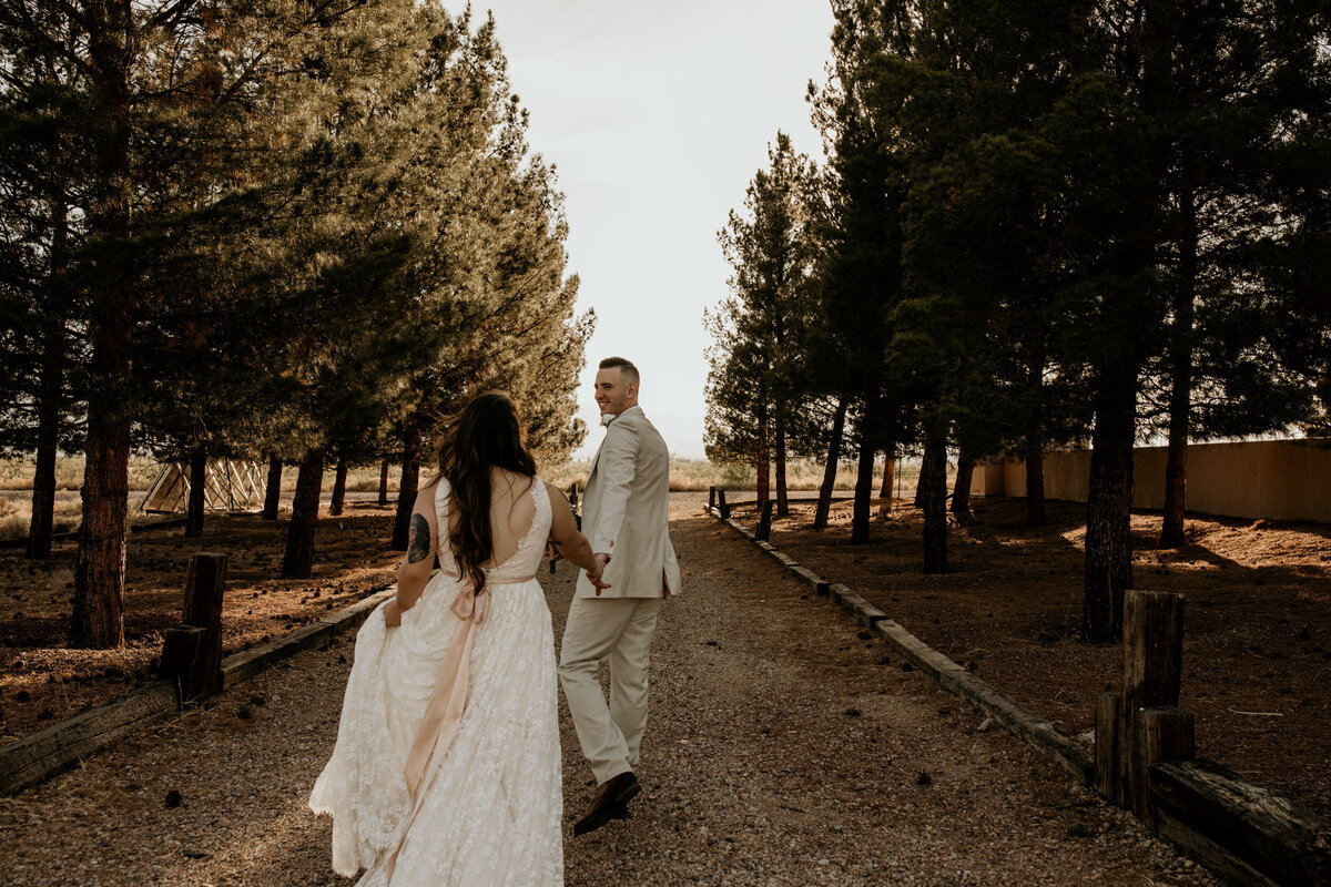 bride and groom walking together through trees in the desert