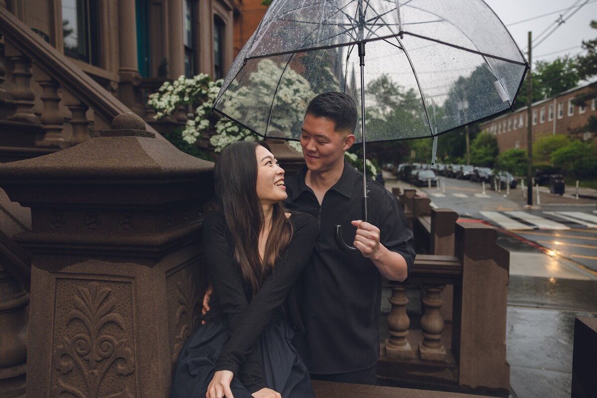 Groom-to-be holding umbrella over laughing bride-to-be