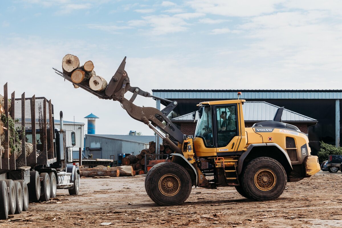 Excavator lifiting logs onto a truck at Devereaux Sawmill.