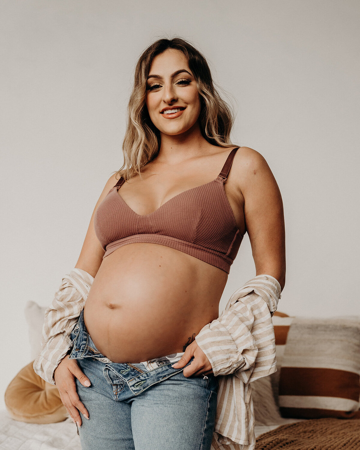 pregnant woman smile at camera wearing an oversized linen shirt and denim with exposed baby bump