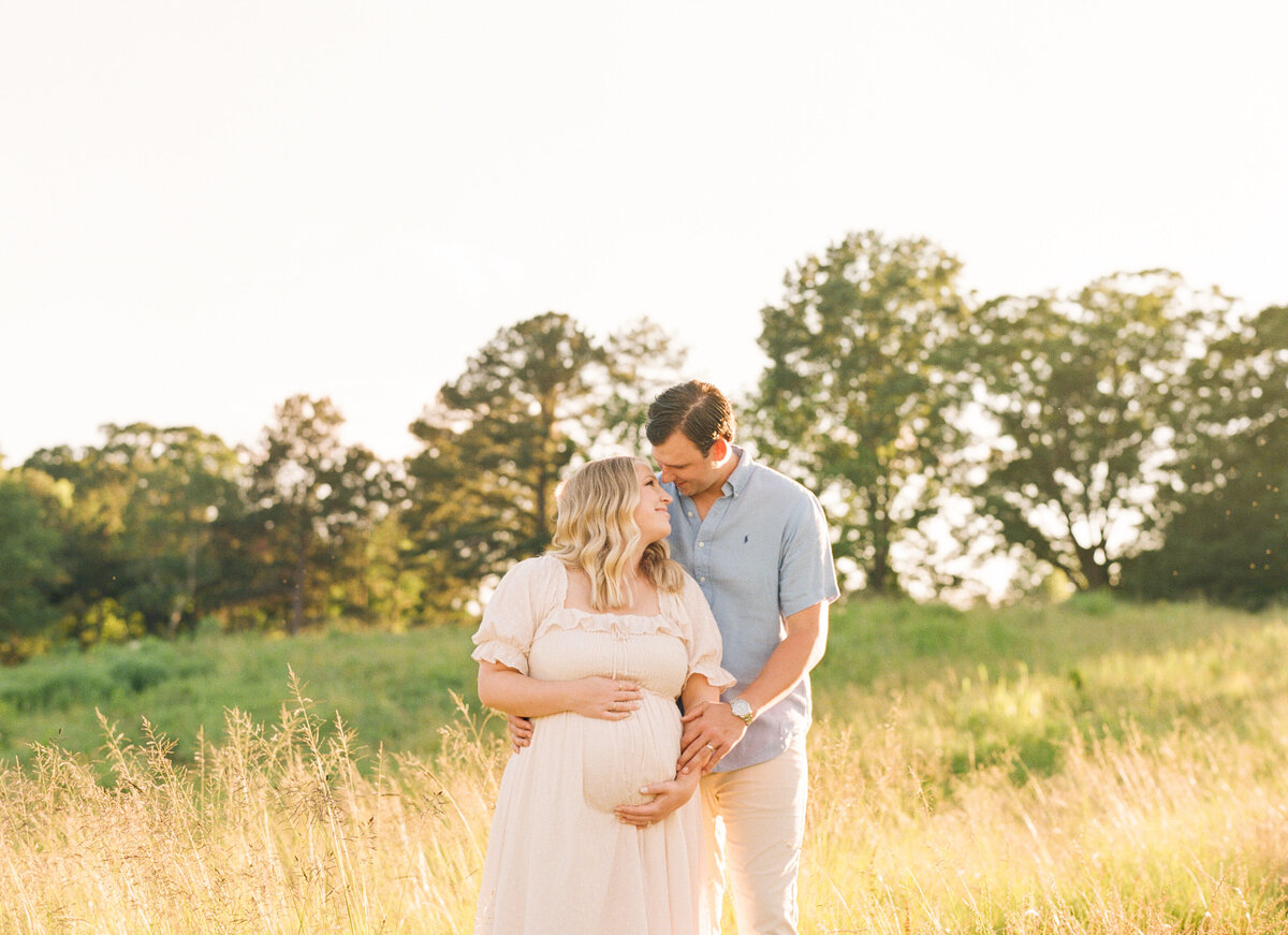 Couple snuggles in a field during their maternity session at the Art Museum in Raleigh NC. Photographed by Raleigh Maternity Photographer A.J. Dunlap Photography.