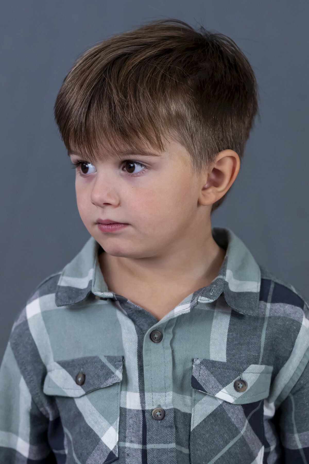 Preschooler looking to his right showing his cute profile wearing a plaid button down shirt