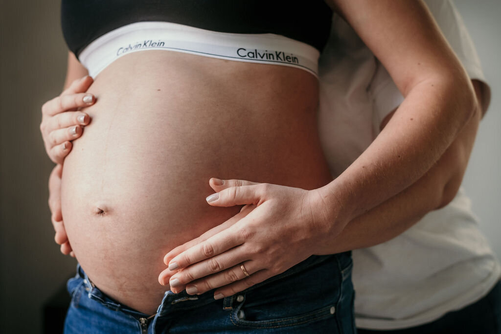 Closeup of a baby bump being hold by the expecting parents.