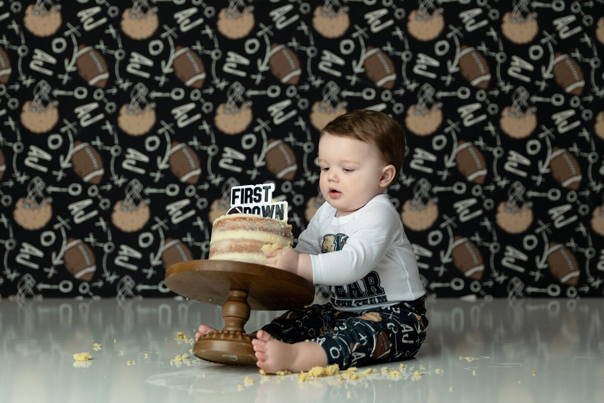 A toddler boy pulls a cake off of a wooden stand while sitting in a studio