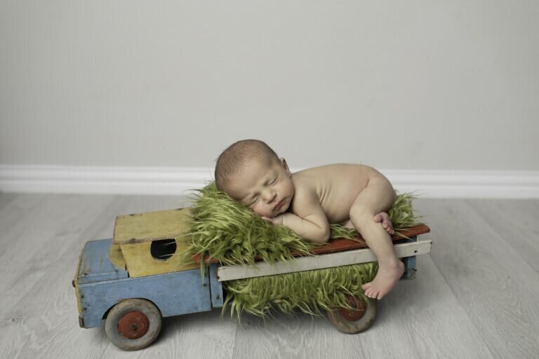 Newborn baby boy peacefully lying in a truck prop, wearing a tiny hat, creating a charming and rustic scene