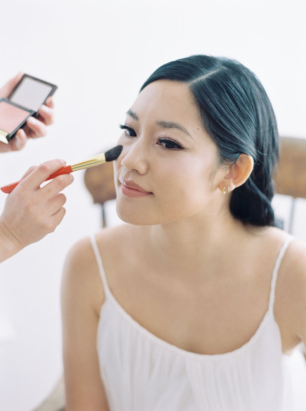 makeup artist applying blush on bride