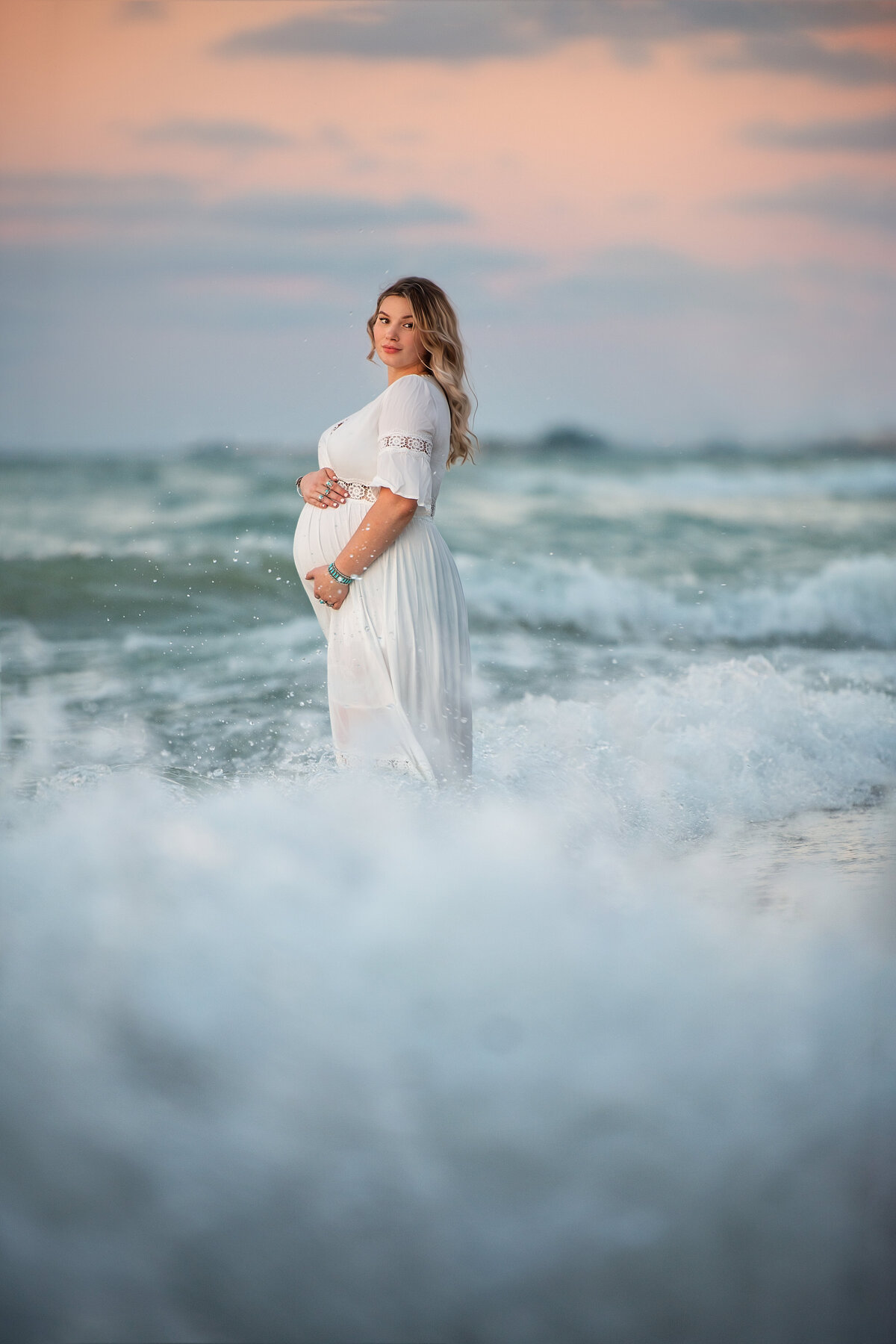 Pregnant mother in white maternity dress  posing in the waves